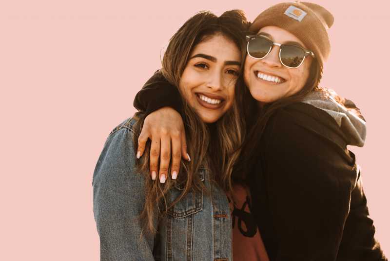 A photo of two young friends hugging each other and smiling.
